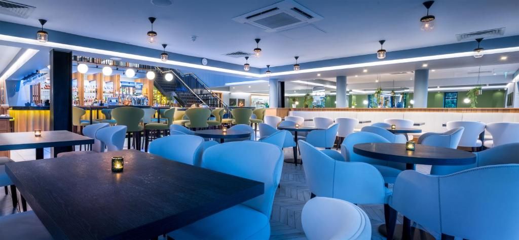 Un restaurante moderno con asientos azules, una zona de bar y una escalera que conduce a un nivel superior.