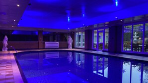 A swimming pool with a tiled deck, a statue, and a view of the outdoors through large windows. - Foxfields Country Hotel (Clitheroe)