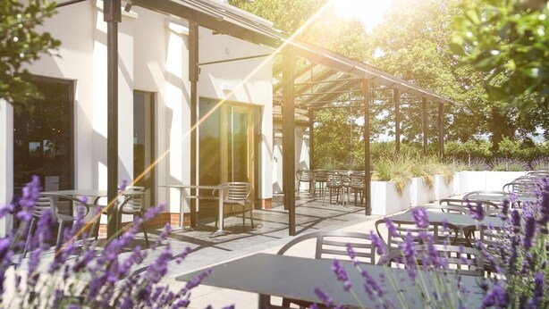 An outdoor seating area with tables and chairs, surrounded by white walls and covered by a pergola. - Foxfields Country Hotel (Clitheroe)