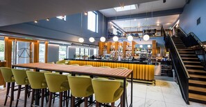 A modern bar area with a wooden bar counter, yellow bar stools, and a staircase leading to an upper level.