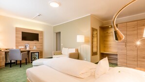 A hotel room with a bed, a desk, a chair, a sofa, a wardrobe, and a lamp.