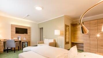 A hotel room with a bed, a desk, a chair, a sofa, a wardrobe, and a lamp.