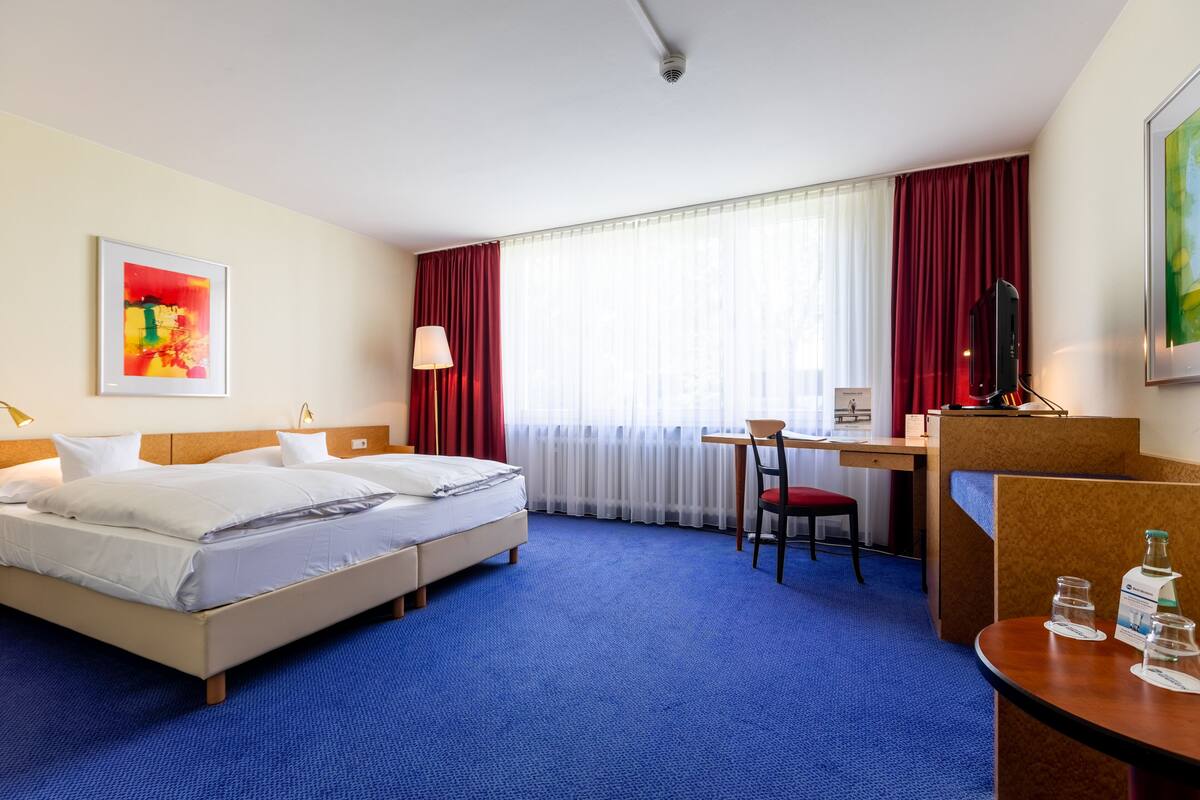A hotel room with a large bed, a desk, a chair, a TV, and a window with curtains.