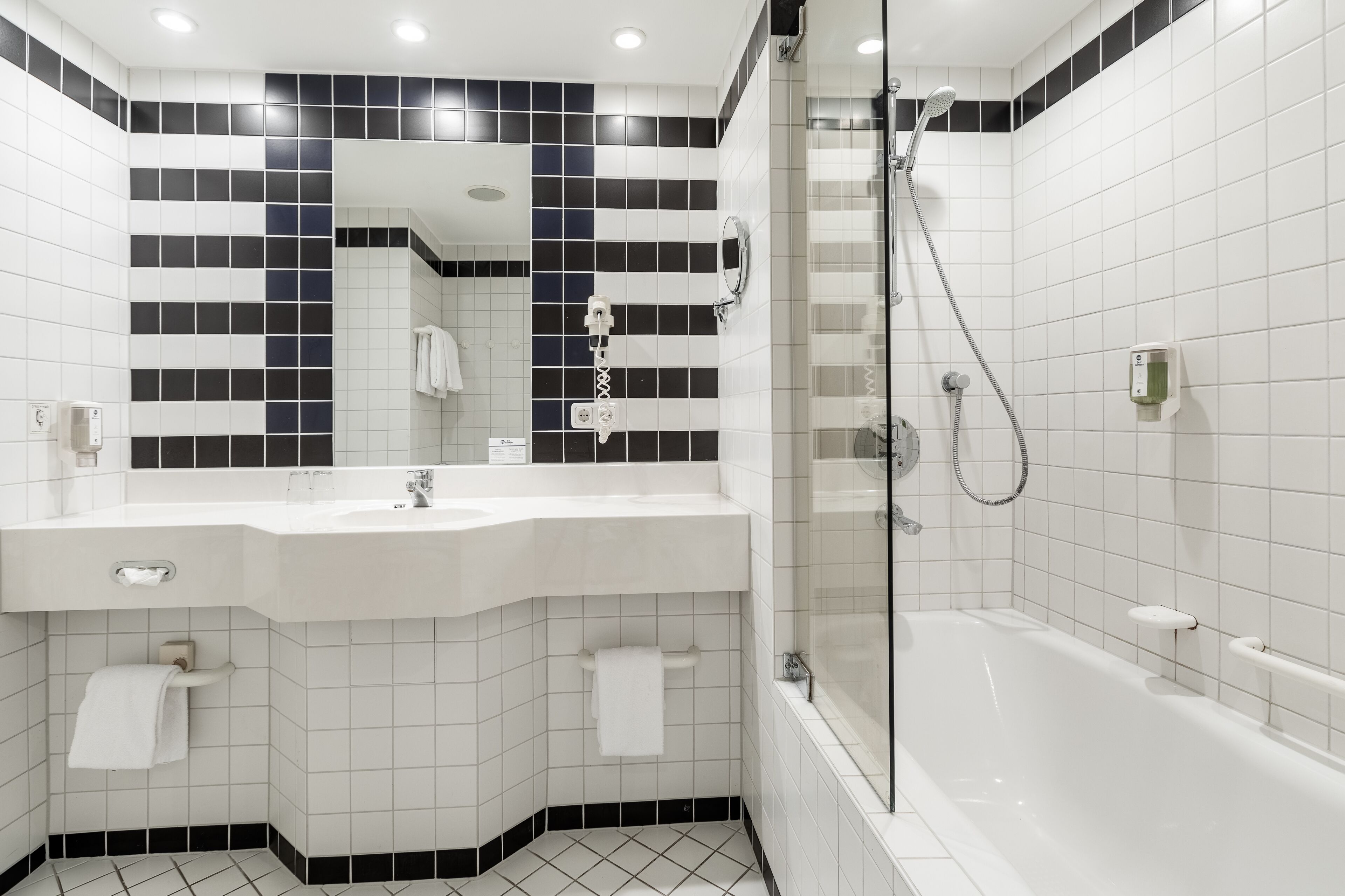 Un baño moderno con lavamanos, espejo y bañera blancos.