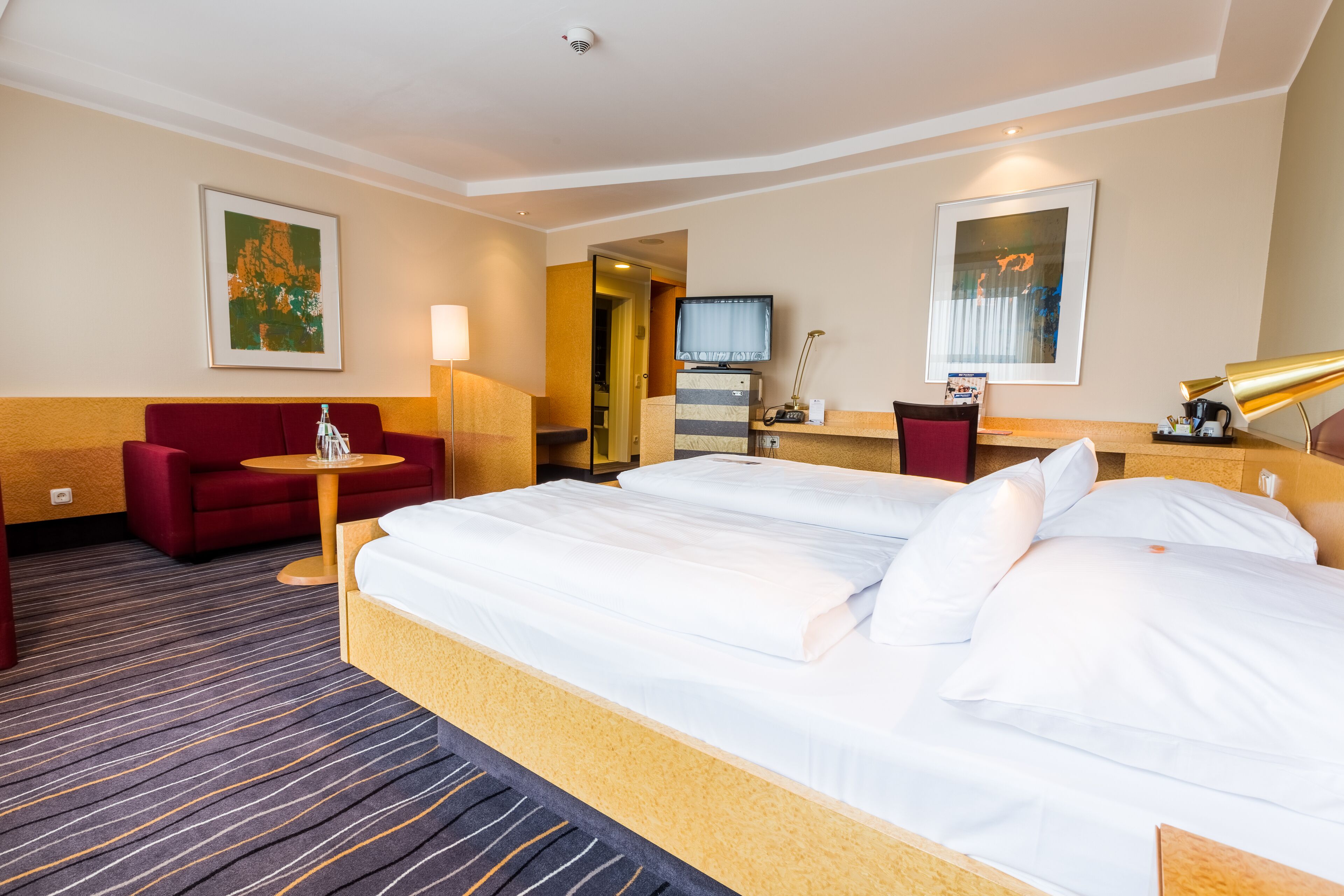 A hotel room with a large bed, a red sofa, a small table, and a TV.