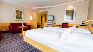 A hotel room with a large bed, a red sofa, a small table, and a TV.