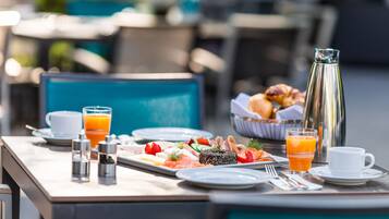 Une table de petit-déjeuner avec des assiettes remplies de nourriture, une cafetière et un verre de jus d’orange.