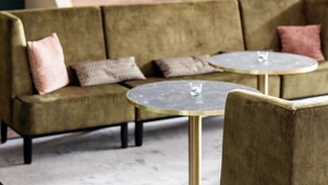 A modern lounge area with a sofa and a small round table, a staircase, and a bar area in the background. - Parkhotel Ropeter (Goettingen)