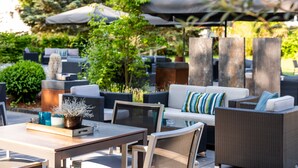 An outdoor seating area with wicker furniture, a wooden table, and umbrellas providing shade. - Parkhotel Ropeter (Goettingen)