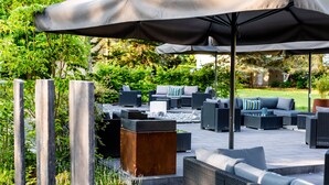 An outdoor patio area with wicker furniture, a large umbrella, and a stone planter.