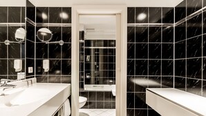 A modern bathroom with black marble tiles, a white sink, and a glass-enclosed shower.
