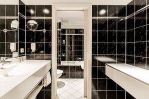 A modern bathroom with black marble tiles, a white sink, and a glass-enclosed shower.