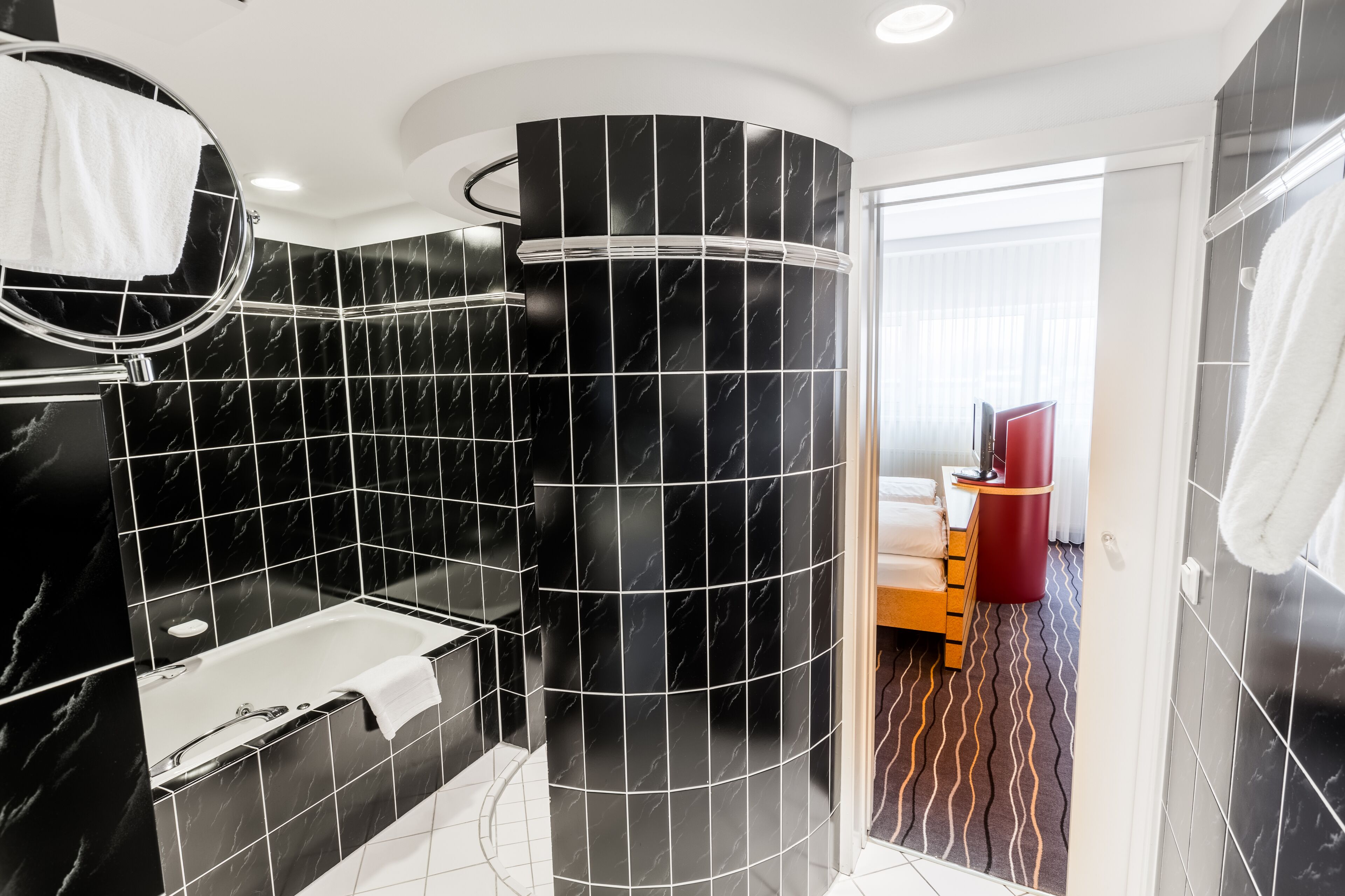 Un baño moderno con baldosas de mármol negro, una bañera, un espejo y un objeto cilíndrico rojo.