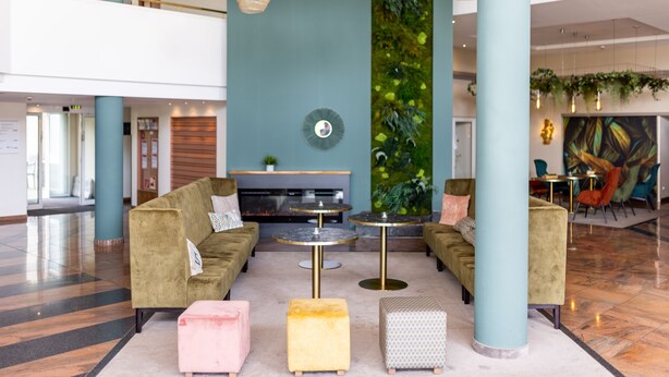 A modern lobby with a green sofa, two round tables, and a vertical garden.