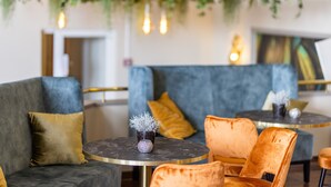 A modern lounge area with a grey sofa, an orange chair, and a round table with a vase of plants. - Parkhotel Ropeter (Goettingen)