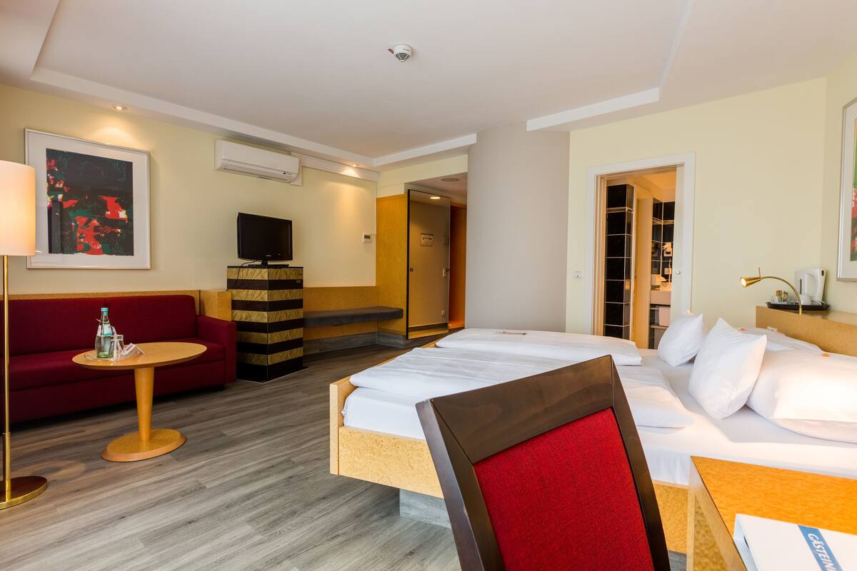 A hotel room with a bed, a sofa, a small table, a TV, and a wardrobe.
