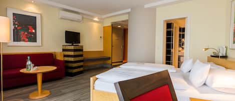 A hotel room with a bed, a sofa, a small table, a TV, and a wardrobe.