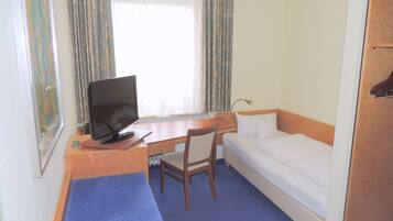 Ein Hotelzimmer mit einem Bett, einem Schreibtisch mit Fernseher, einem Sessel und einem Fenster mit Vorhängen.