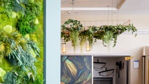 A modern lobby with a green vertical garden, a mural, a round table with chairs, and a staircase. - Parkhotel Ropeter (Goettingen)