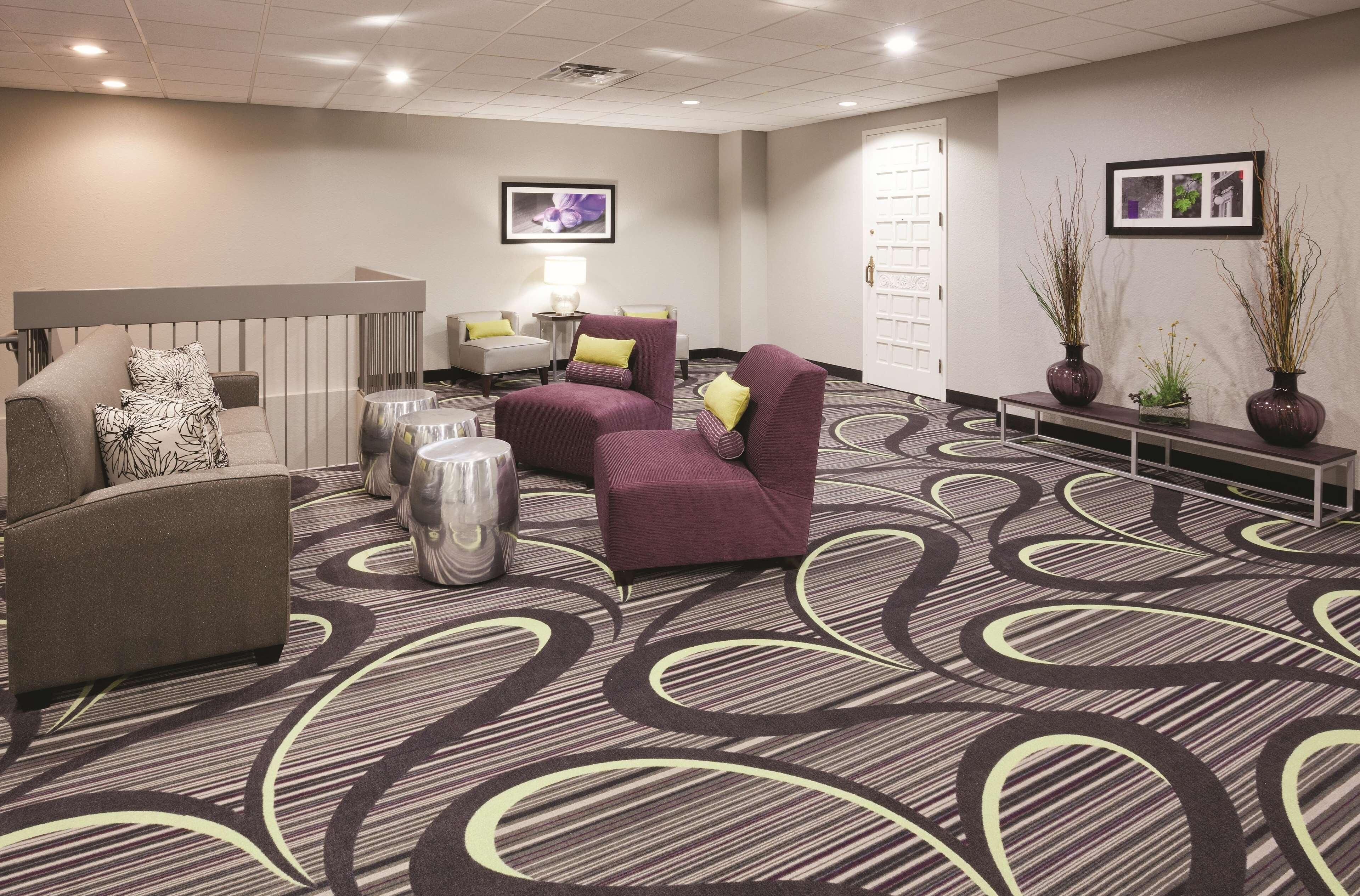 A hotel lobby with a patterned carpet, seating area with armchairs and a sofa, a reception desk, and wall-mounted artwork.