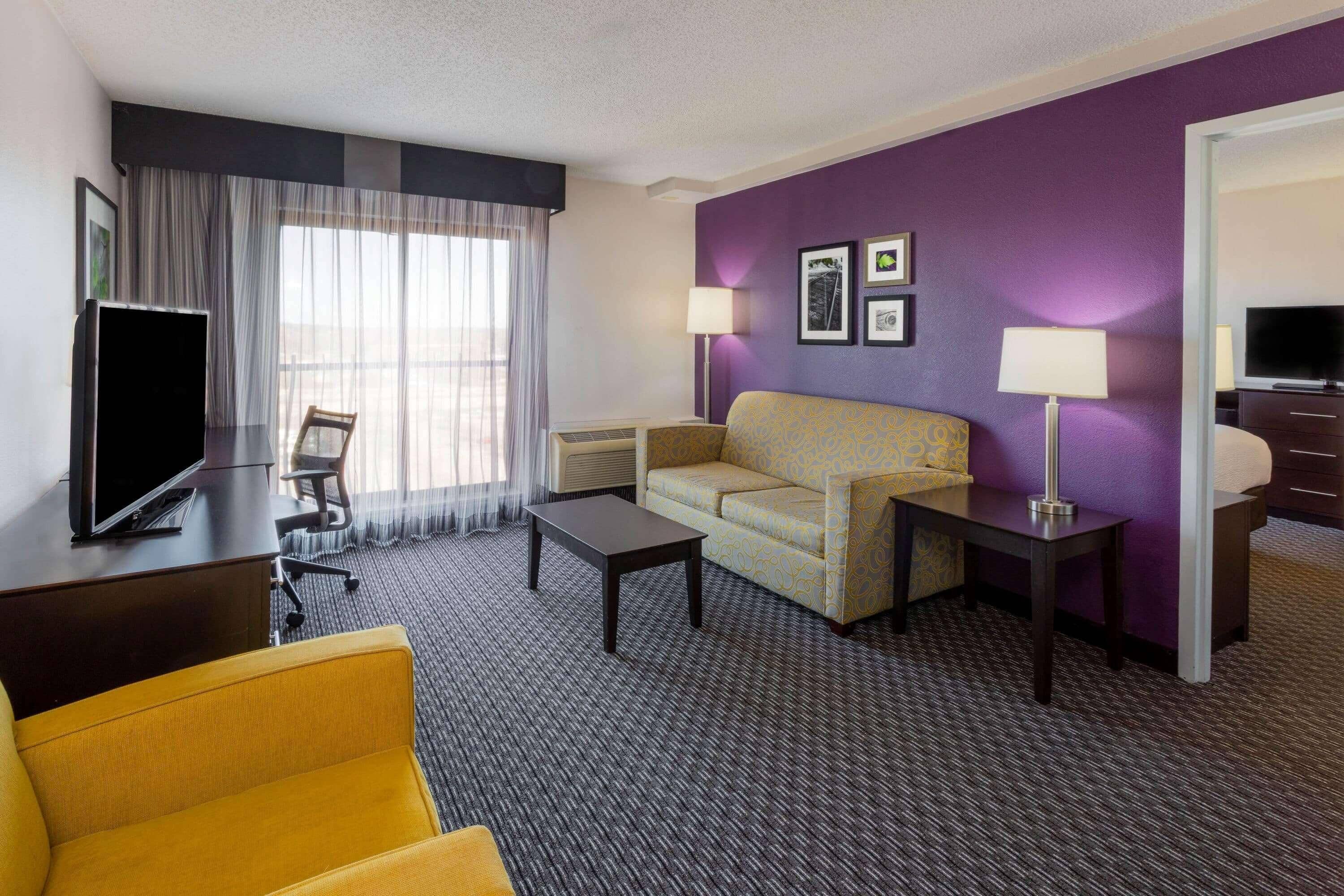 A hotel room with a sofa, armchair, television, and two lamps.