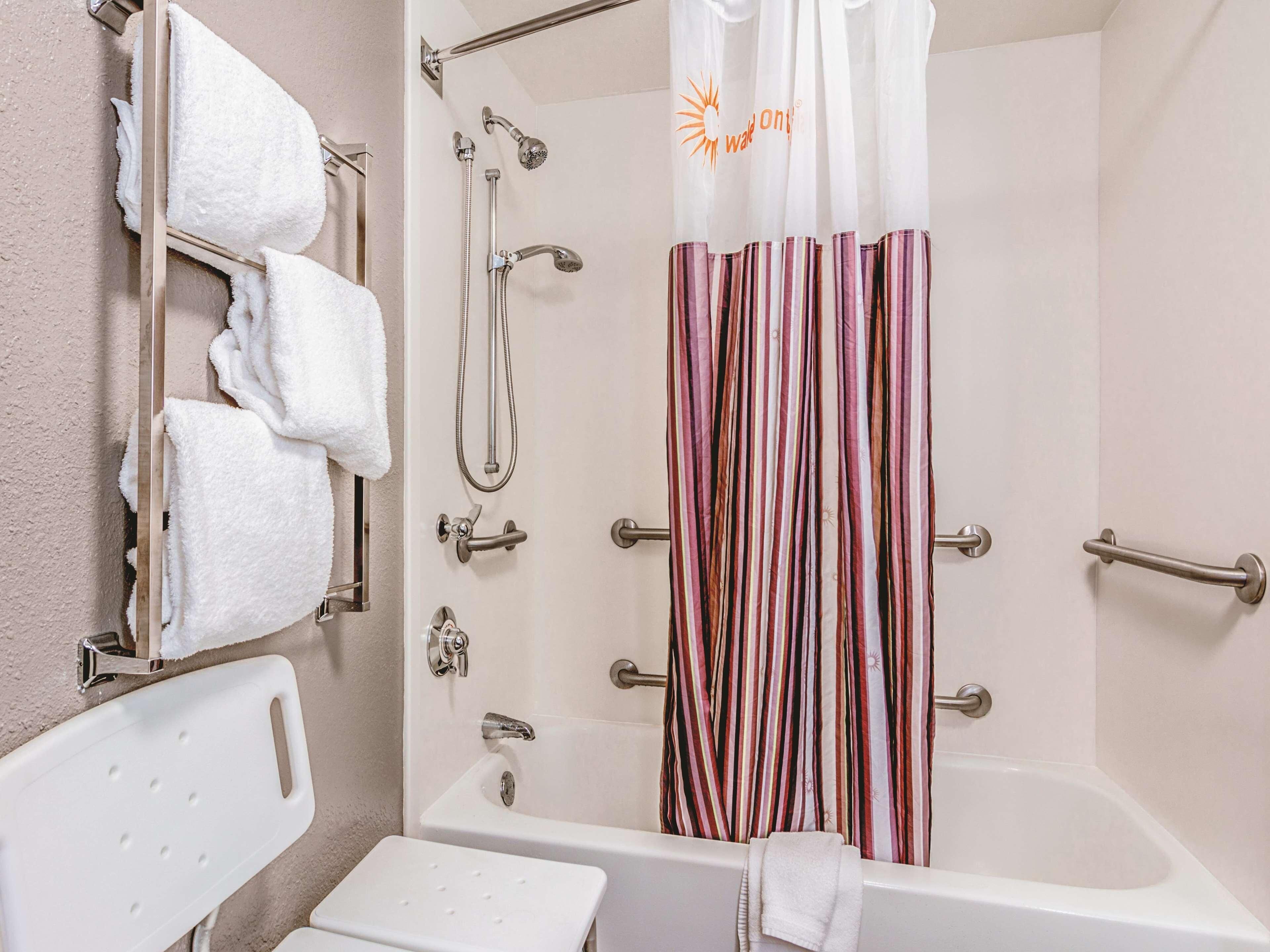 A bathroom with a shower, a bathtub, a towel rack, and a handrail.