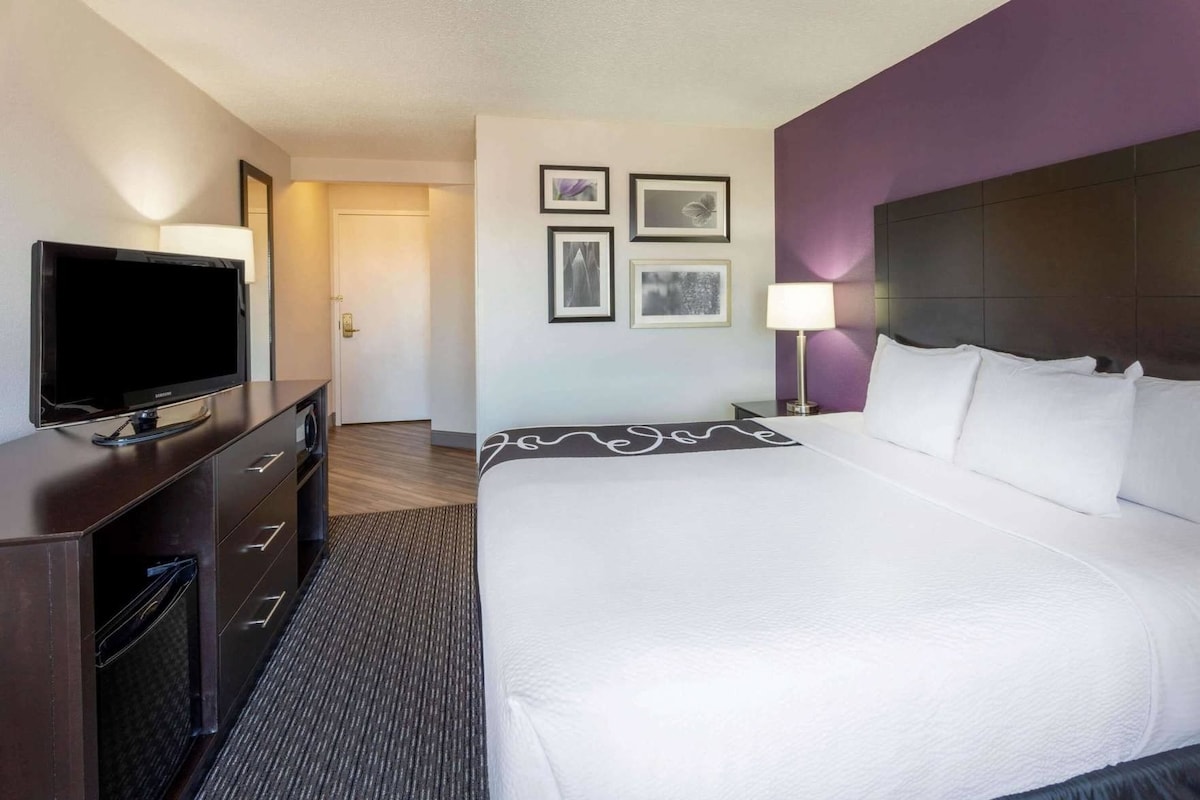 A hotel room with a bed, a TV on a dresser, a door, and framed pictures on the wall.