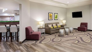 Eine Hotelhalle mit einer Couch, Sesseln, einem Fernseher und Kunstwerken an der Wand.