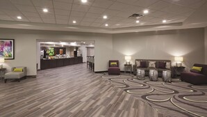 Eine Hotelhalle mit einer Rezeption, einer Sitzecke mit Sesseln und Beistelltischen sowie einem gemusterten Teppich.