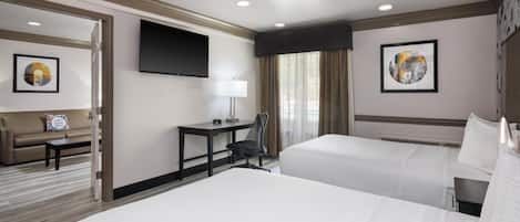Ein Hotelzimmer mit zwei Betten, einem Schreibtisch, einem Sessel, einem Fernseher und Bildern an den Wänden.