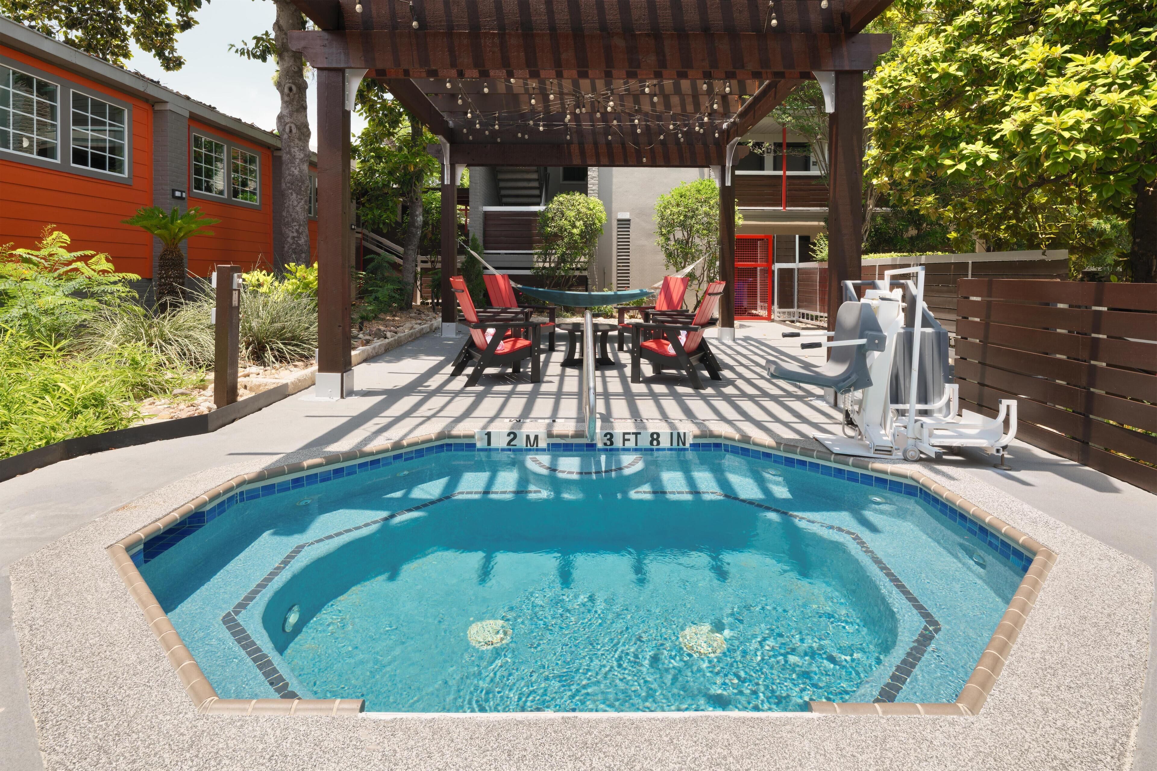 Une piscine rectangulaire dont le bord est recouvert de carreaux, entourée d’une terrasse couverte avec des chaises longues rouges et blanches.