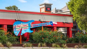 A building with a red facade, a large guitar-shaped sign with the text "KEEPIN IT ANOTIN" and "Aiden by Best Western" on the roof, surrounded by greenery and flowers.