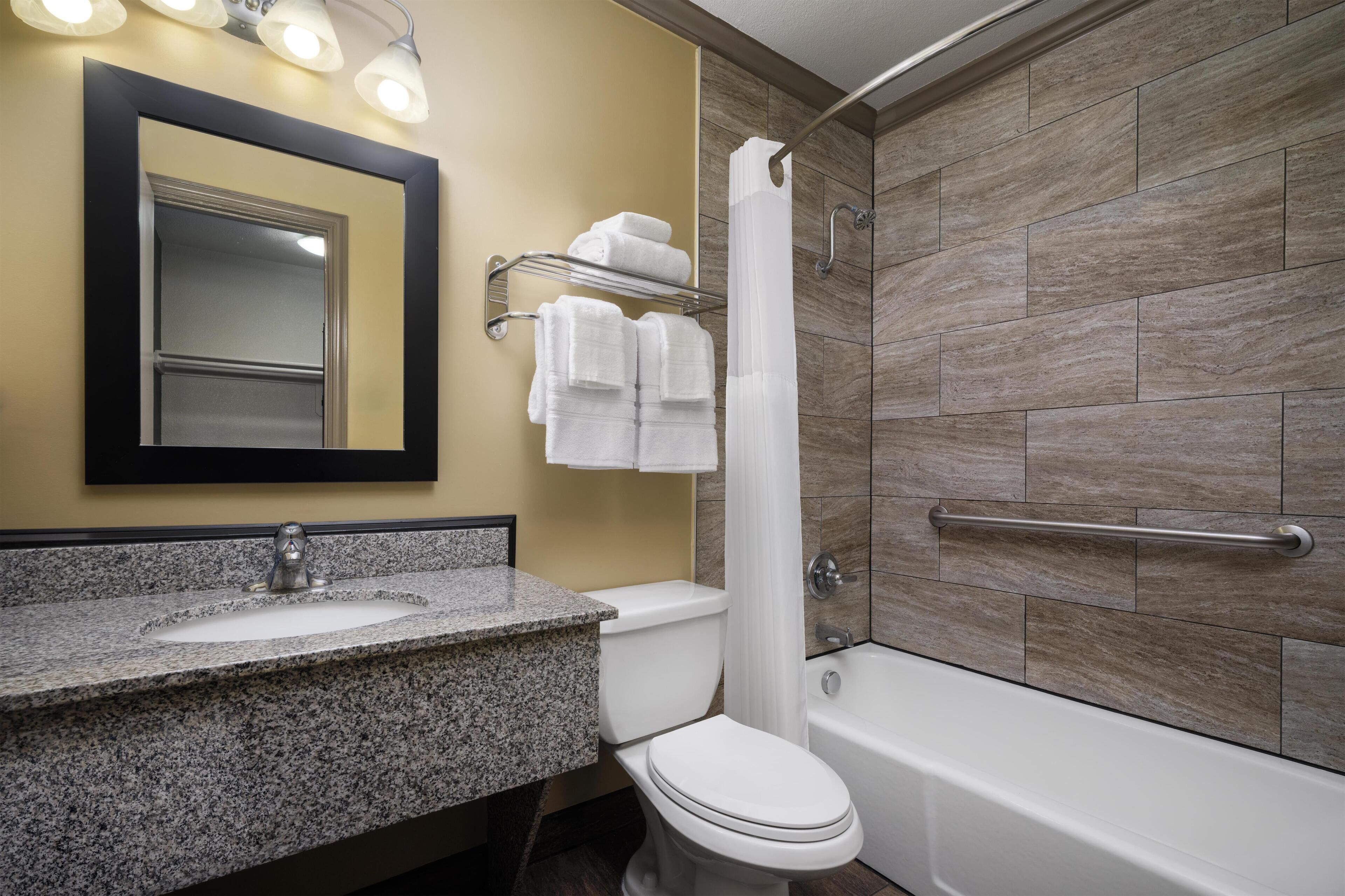 A bathroom with a granite countertop sink, a white toilet, a bathtub, and a shower curtain.