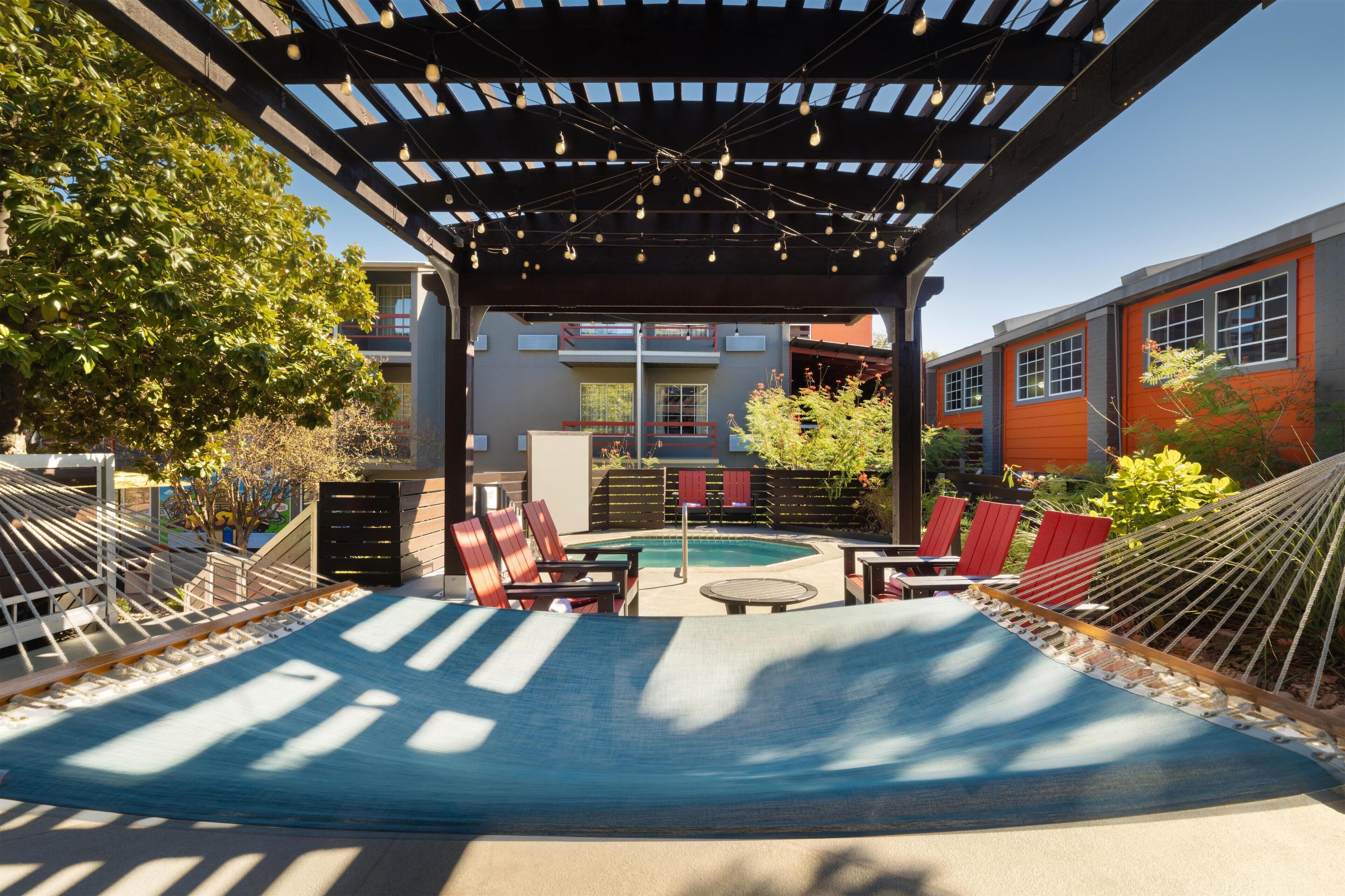 A covered outdoor area with a hammock, lounge chairs, and a pool.