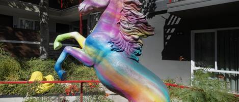 A colorful horse statue in a garden setting with a building in the background.