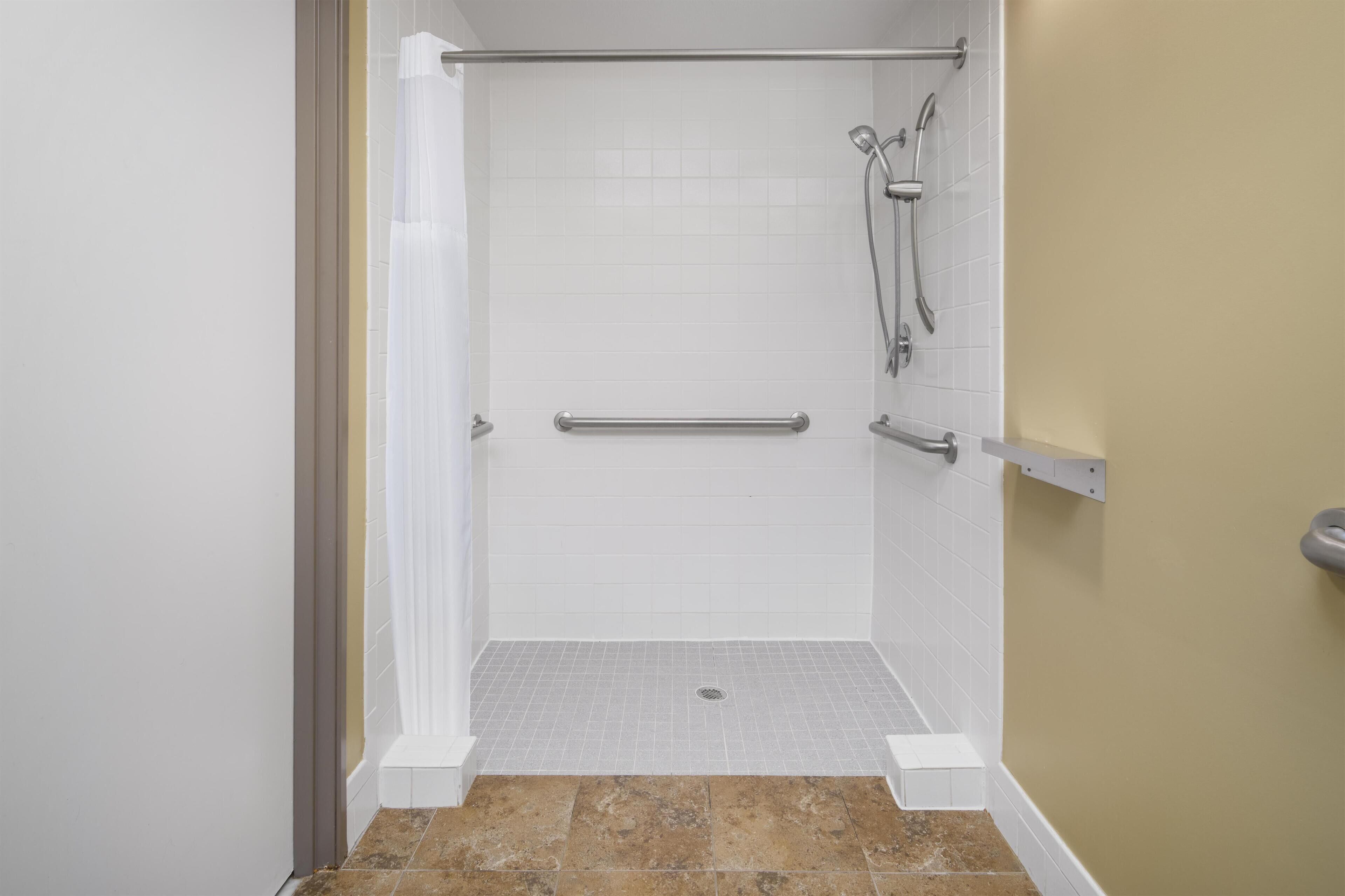 Una ducha a nivel con paredes de azulejos blancos, una pared de acento color beige y piso de azulejos.