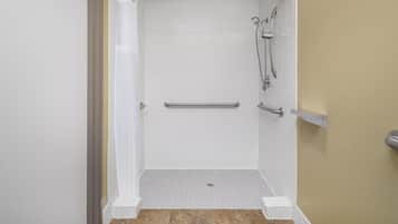 Una ducha a nivel con paredes de azulejos blancos, una pared de acento color beige y piso de azulejos.