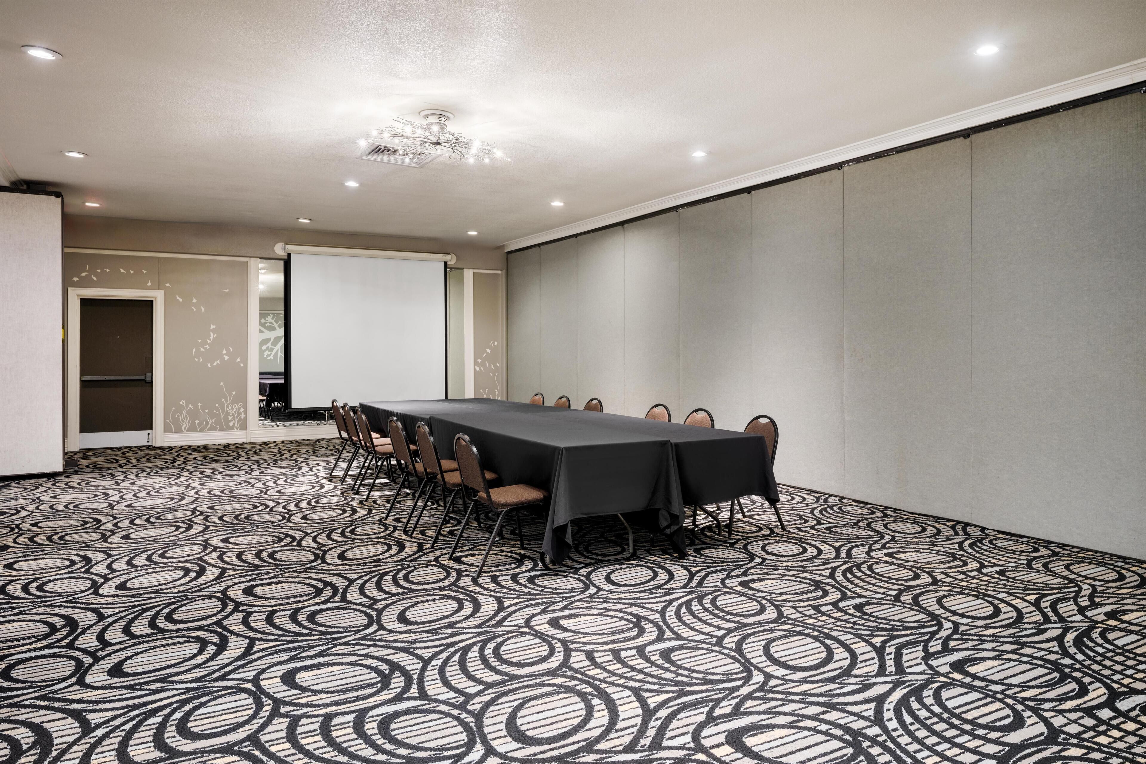 A conference room with a long table, chairs, and a projector screen.