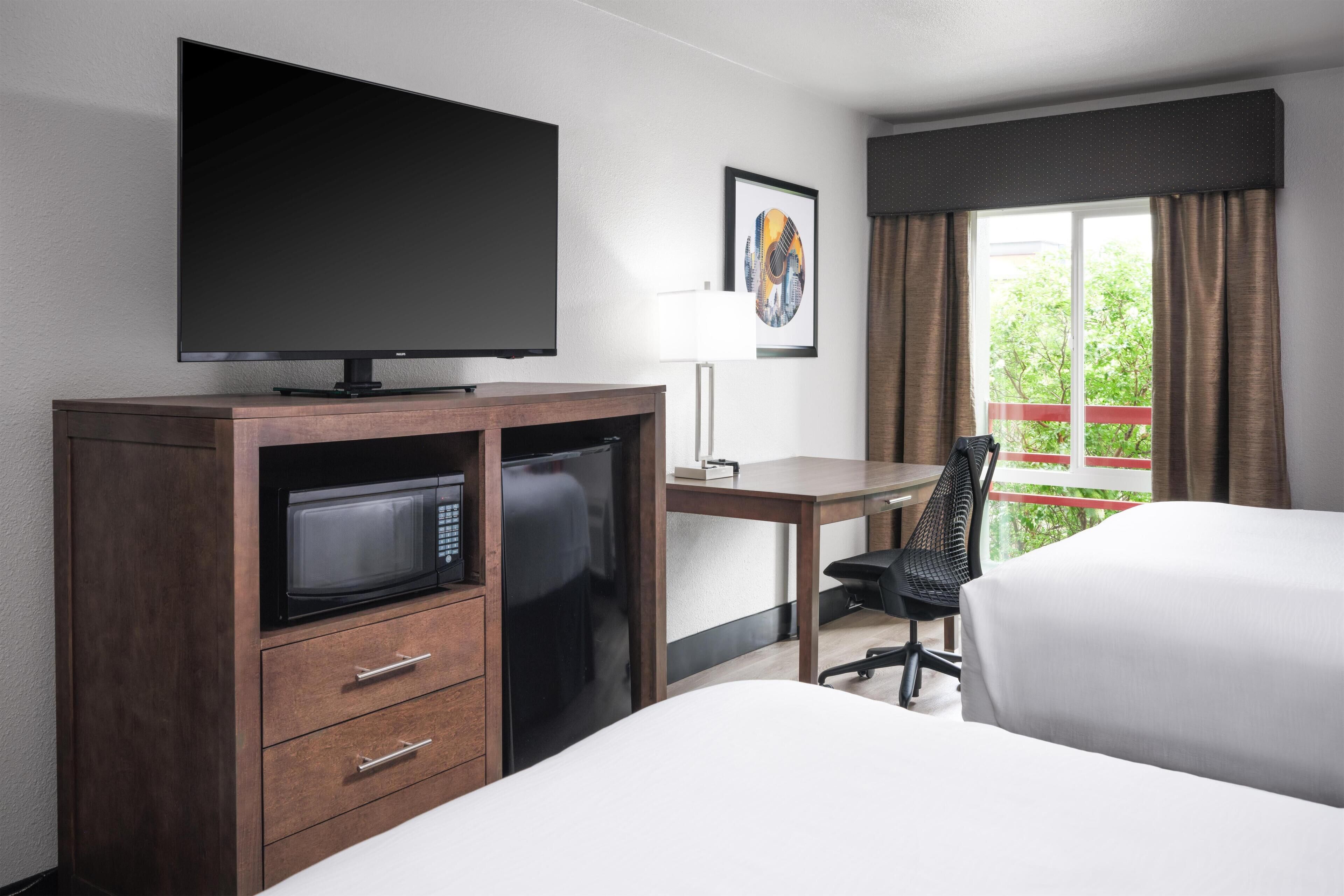 A hotel room with a bed, a desk, a television, a microwave, and a chair.