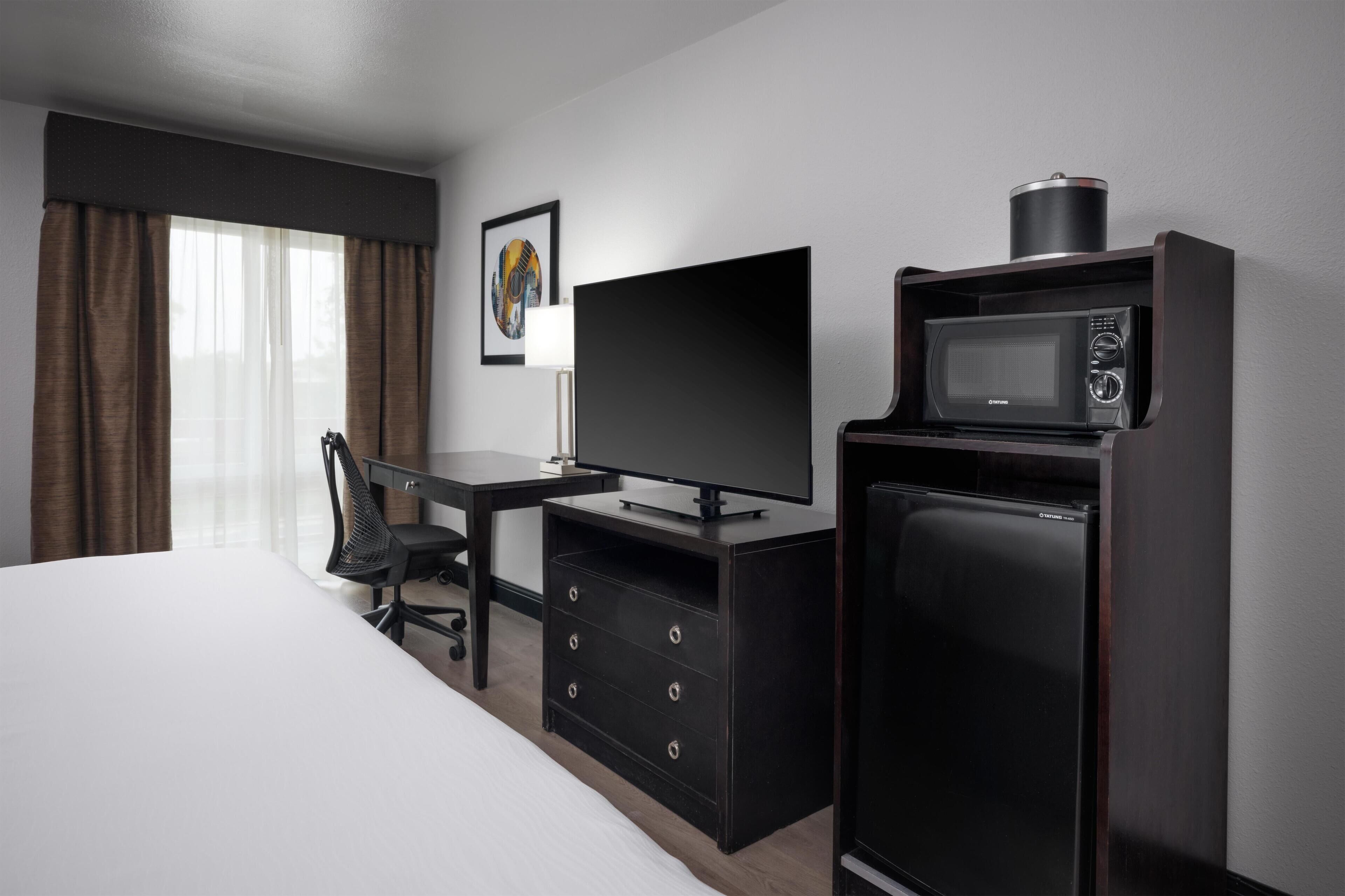 A hotel room with a bed, a desk with a flat-screen TV, a microwave, and a dresser.