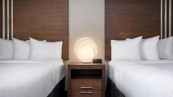 Habitación de hotel con dos camas, una mesita de noche con una lámpara circular y un cabecero de madera.