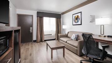 Una habitación de hotel moderna con suelo de madera, un sofá, un escritorio, una silla, un televisor y una puerta.