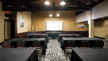 A conference room with tables and chairs, a projector screen, and a brick wall.