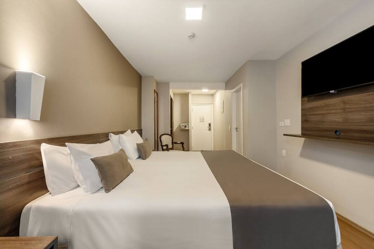 Une chambre d’hôtel avec un grand lit, un téléviseur fixé au mur et une tête de lit en bois.