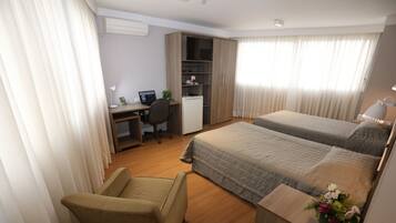 A hotel room with a bed, a desk, a chair, a wardrobe, and a small table with a vase of flowers.