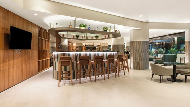 Een moderne bar met een houten toog, meerdere krukken en een flatscreen televisie aan de muur.