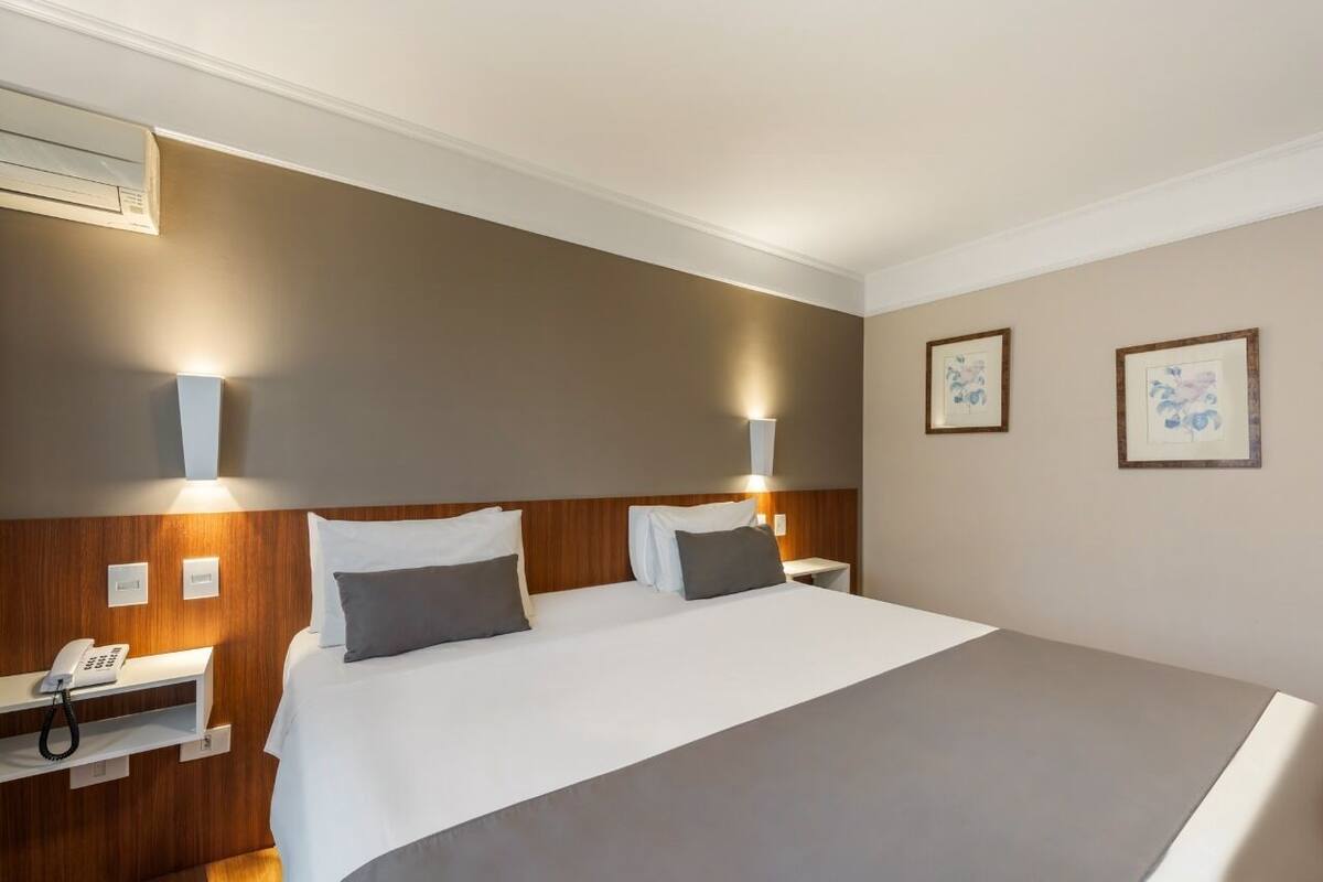 Une chambre d’hôtel avec un grand lit, des tables de chevet, un téléphone et des lampes fixées au mur.