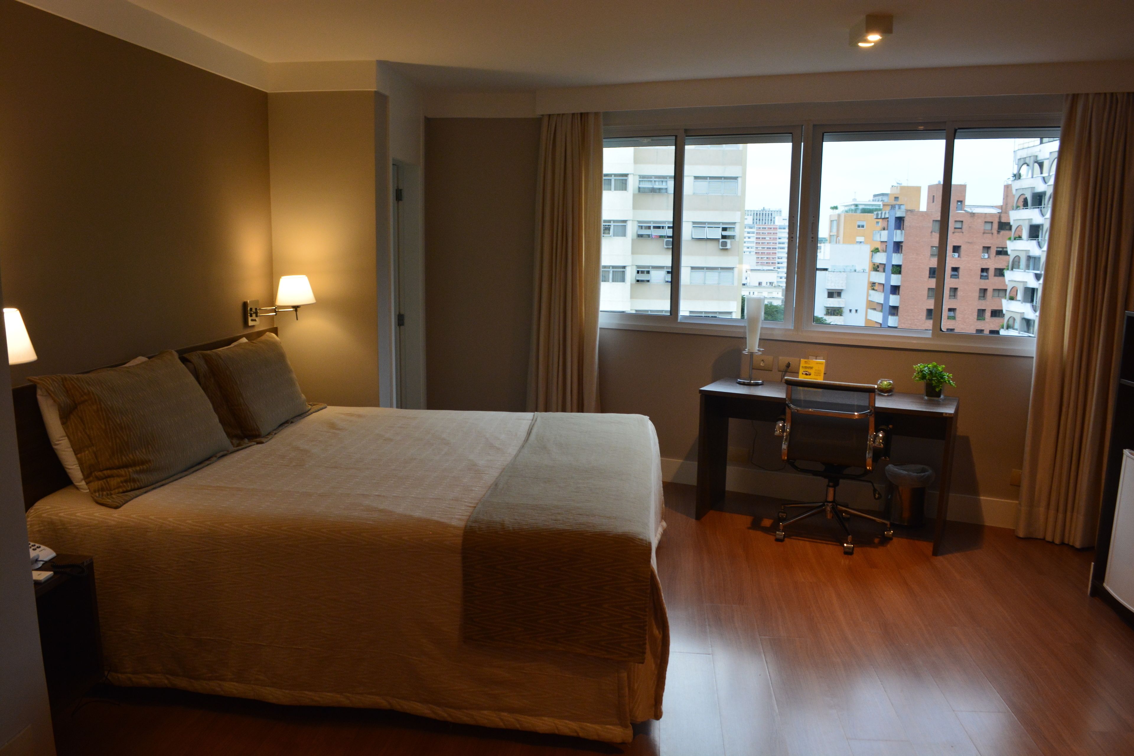 Habitación de hotel con una cama grande, un escritorio con una silla y una ventana con vistas a la ciudad.