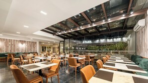 Een modern restaurant met een hoge plafond, glazen wanden en uitzicht op groen buiten.