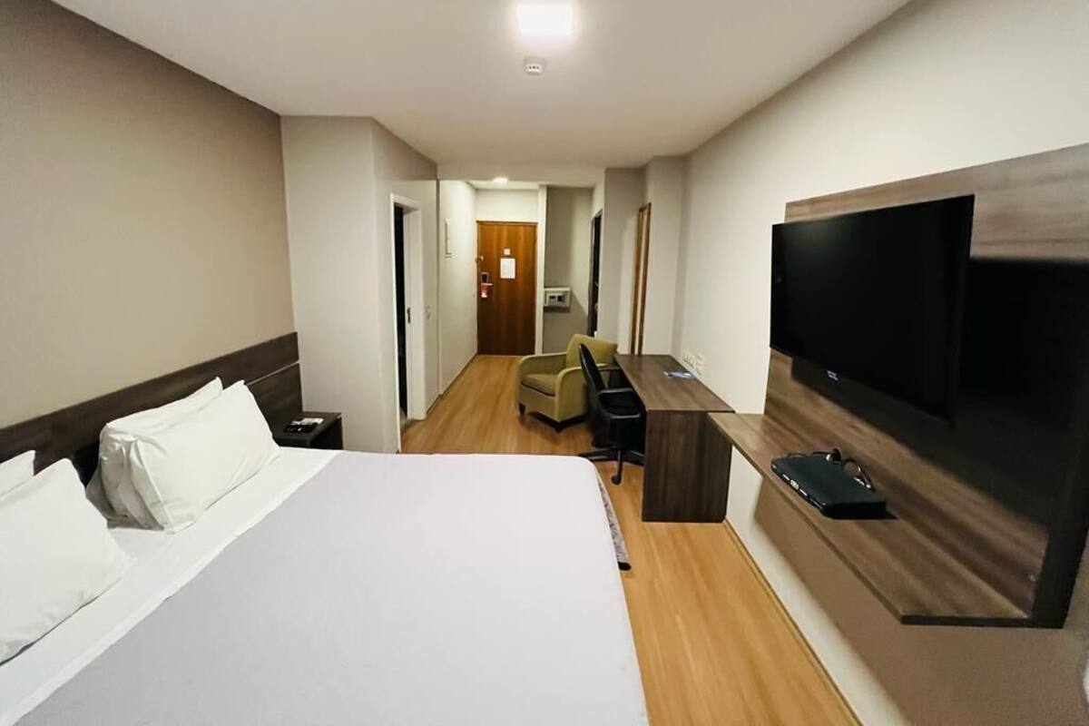 Une chambre d’hôtel équipée d’un lit, d’un bureau, d’une chaise, d’une télévision et d’une porte donnant sur un couloir.